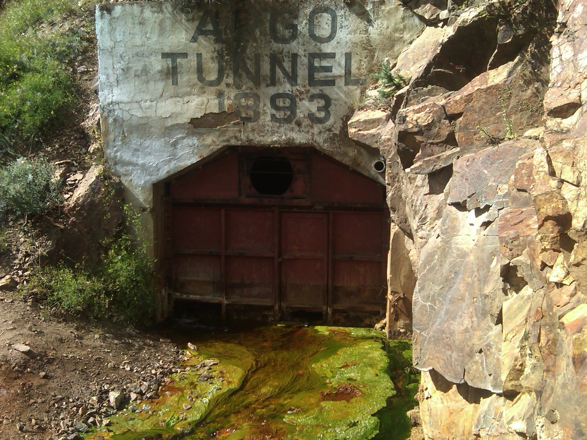 Portal of the Argo Tunnel marked 1893 with mineral-stained water